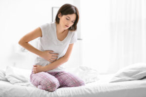 young woman sitting on bed experiencing abdominal pain