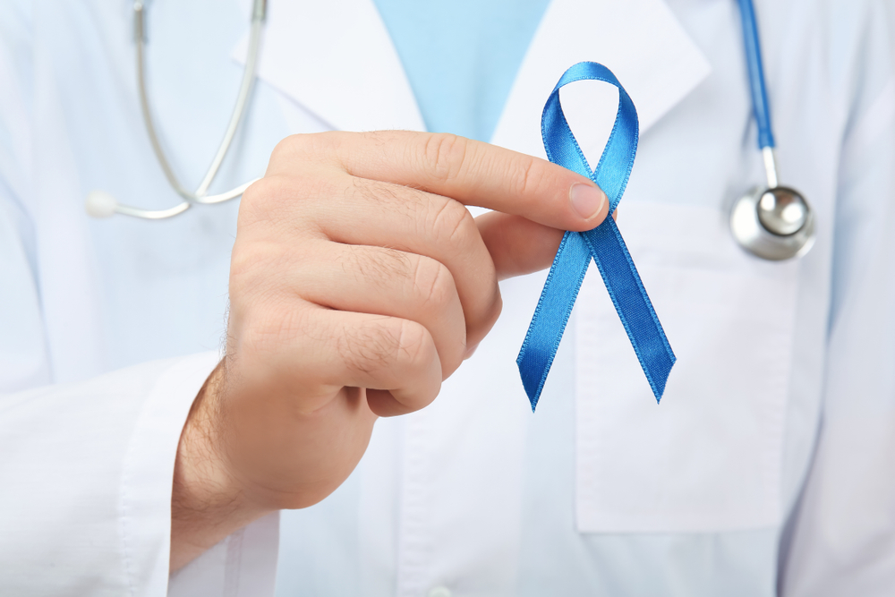Doctor holding blue ribbon, closeup. Cancer awareness concept