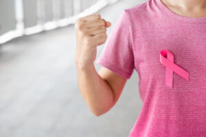 Woman with pink shirt and breast cancer ribbon showing muscles. 