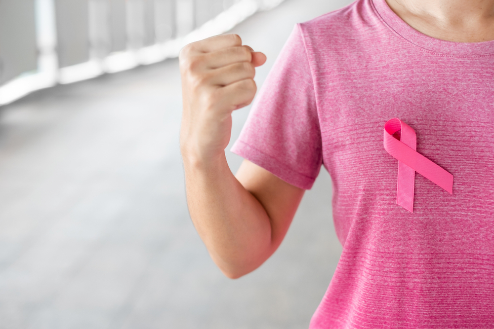 Woman with pink shirt and breast cancer ribbon showing muscles.